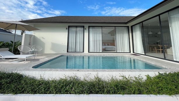 Une maison moderne dotée d’une piscine, de grandes portes-fenêtres coulissantes et d’un patio aménagé avec du mobilier d’extérieur.