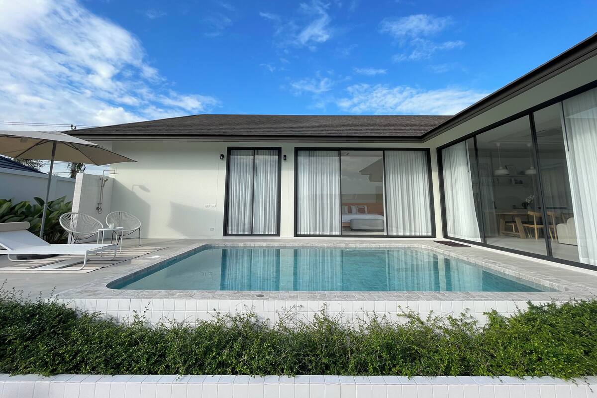 Ein modernes Haus mit Swimmingpool, großen Schiebeglasfenstern und einer Terrasse mit Gartenmöbeln.
