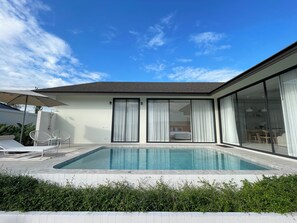 A modern house with a swimming pool, large sliding glass doors, and a patio area with outdoor furniture.