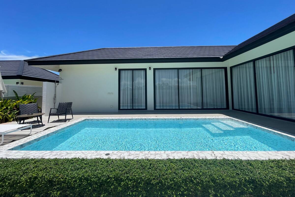 Ein modernes Haus mit Swimmingpool, überdachter Terrasse und großen Schiebeglastüren.