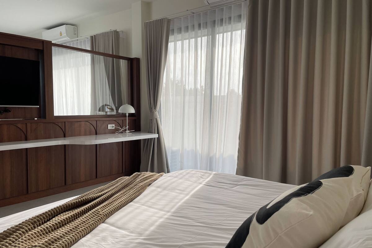 Ein Hotelzimmer mit einem Bett, einem Nachttisch, einer Lampe, einem Spiegel und einem Fenster mit Vorhängen.