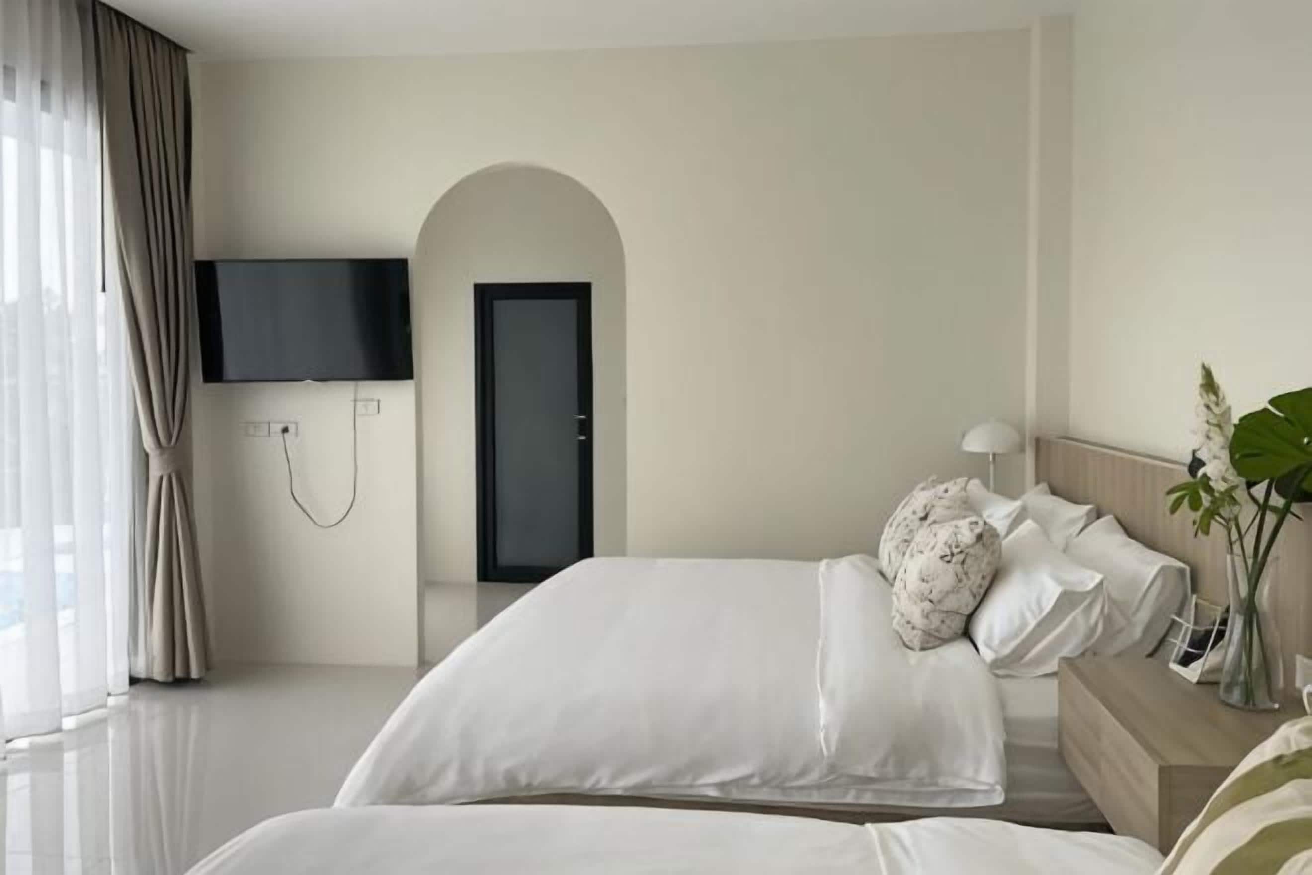 Ein Hotelzimmer mit Bett, Fernseher, Tür und Pflanze.