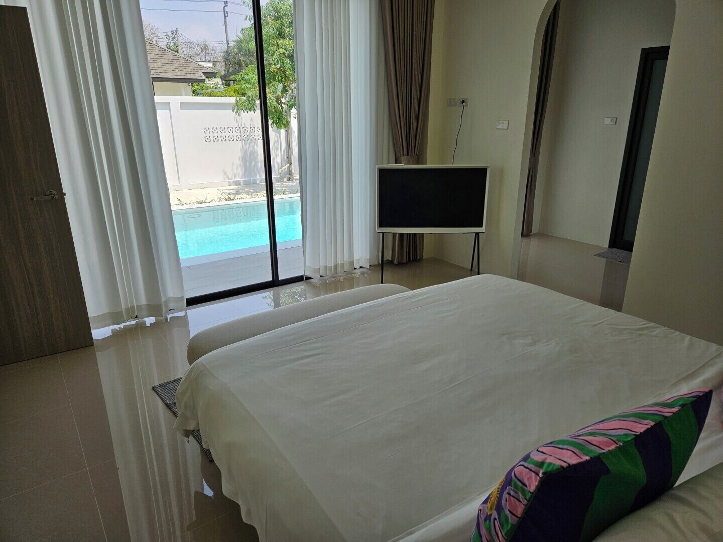 A hotel room with a large bed, a TV, and a view of a swimming pool.