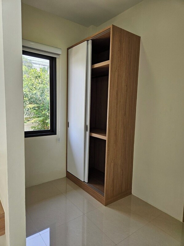 A room with a wardrobe, a window, and a tiled floor.