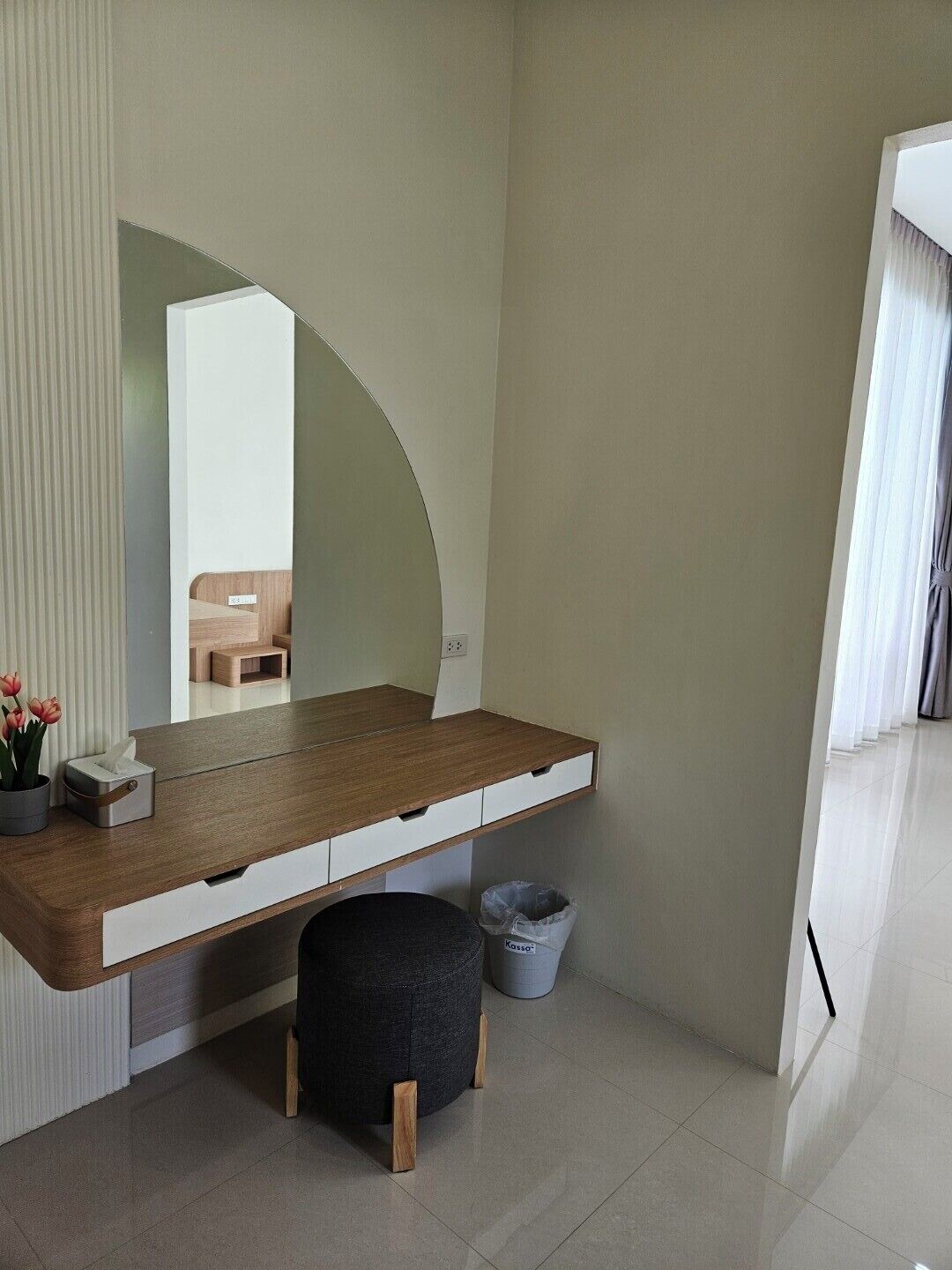 Une chambre à coucher moderne avec une coiffeuse en bois, un miroir, un petit tabouret et une poubelle.
