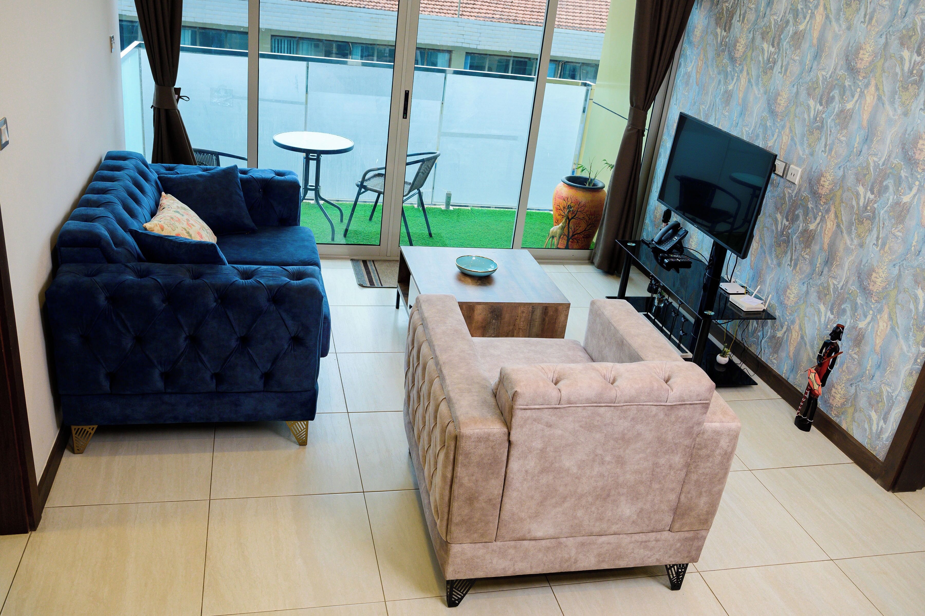 A living room with a blue sofa, a pink armchair, a small table, and a TV.