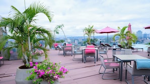 Eine Dachterrasse mit Sitzgelegenheiten im Freien, Topfpflanzen und Blick auf die Stadt.
