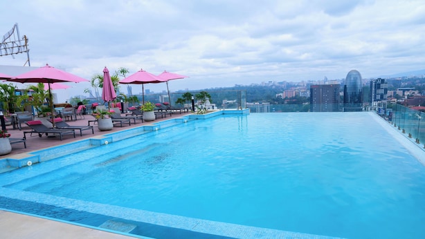 Ein Infinity-Pool auf dem Dach mit Liegestühlen und Sonnenschirmen, mit Blick auf die Stadt.