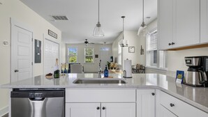 Een moderne keuken met witte kasten, roestvrijstalen apparatuur en een groot eiland inclusief vaatwasser.