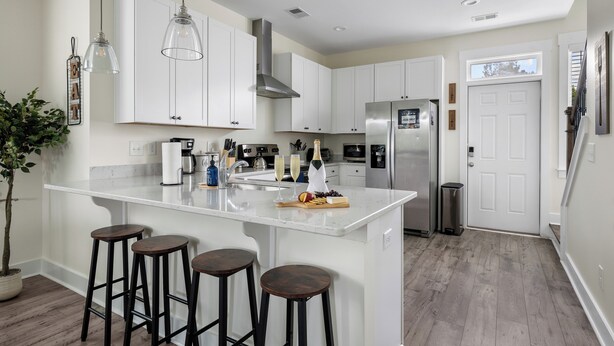 Een moderne keuken met witte kastjes, een centraal eiland met krukken, roestvrijstalen apparatuur en hanglampen.