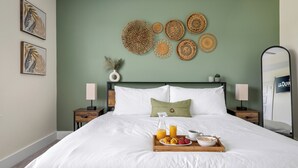 Een net opgemaakt bed met een dienblad ontbijtartikelen, een groene muur met wanddecoratie en een spiegel aan de rechterkant.