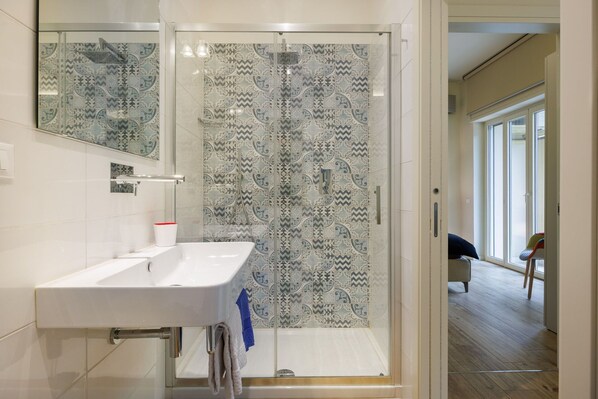 Ein modernes Badezimmer mit Dusche, weißem Waschbecken und gemusterten Fliesen.