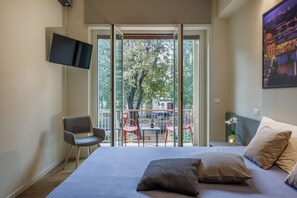 Ein Schlafzimmer mit einem Bett, Kissen, einem Fernseher, einem Sessel und einem Balkon mit Tisch und Stühlen.