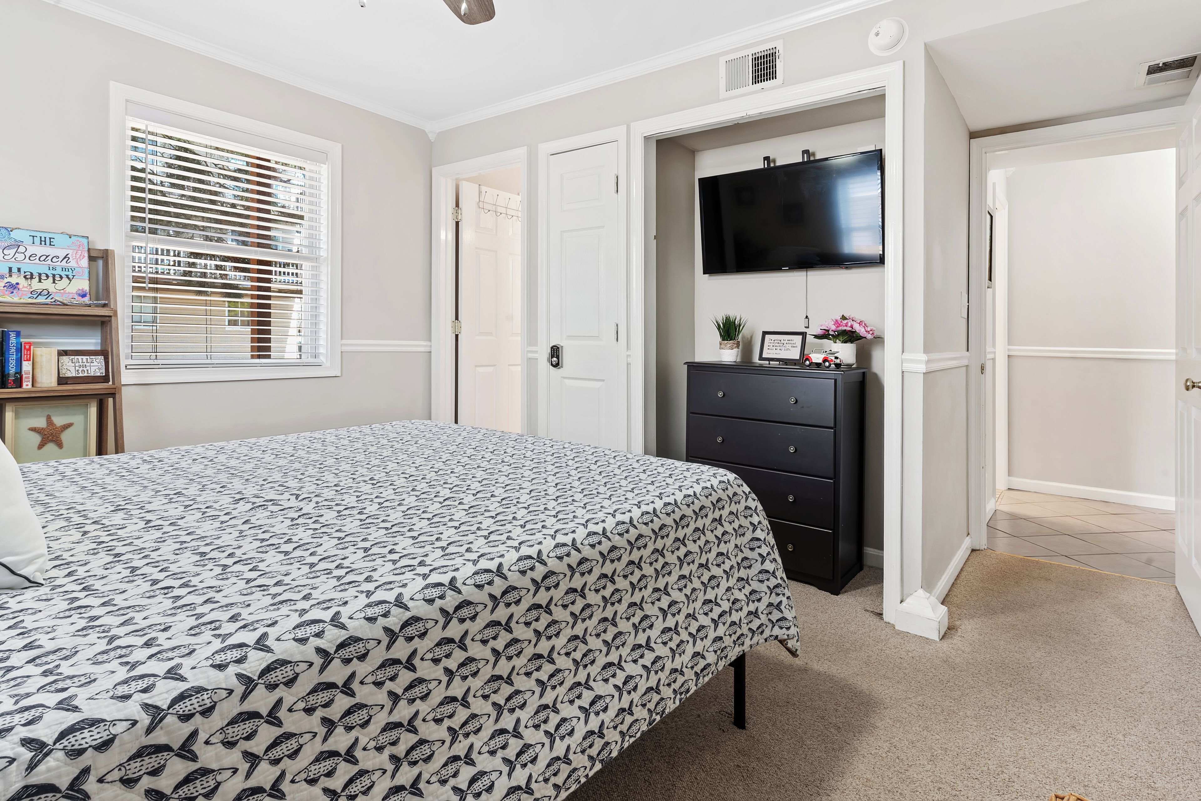 A bedroom with a bed, a dresser, a television, and a door leading to another room.