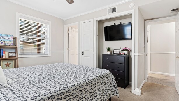 Un dormitorio con cama, cómoda, televisor y puerta que da a otra habitación.