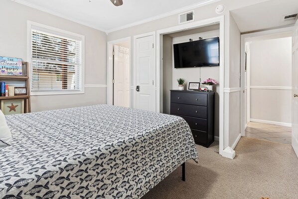 A bedroom with a bed, a dresser, a television, and a door leading to another room.