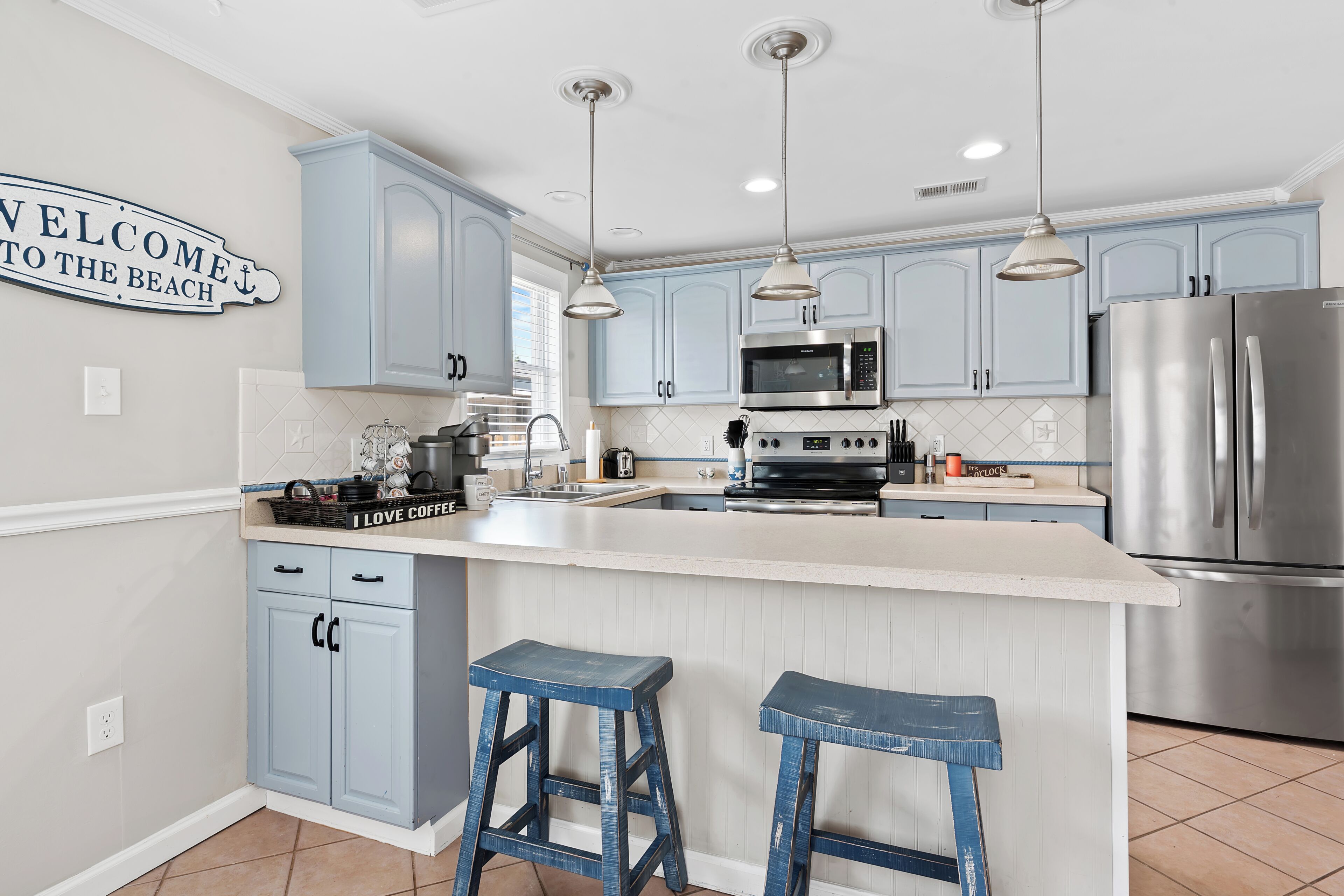 Una cocina moderna con armarios azul claro, electrodomésticos de acero inoxidable y una isla central con taburetes.