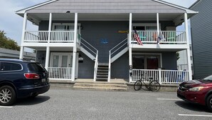 Un edificio de dos plantas con un balcón en el piso superior, una bicicleta estacionada adelante y una bandera a la derecha.