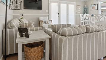 A living room with striped sofas, a small table, a television, and a wicker basket.