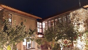 A stone building with large windows and a balcony, surrounded by trees and plants.