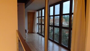 Una habitación amplia con ventanas grandes, suelo de madera y un pilar metálico.