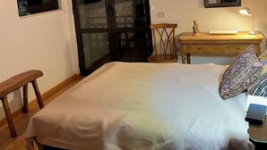 A bedroom with a bed, a wooden bench, a desk with a lamp, a mirror, and a sliding glass door.