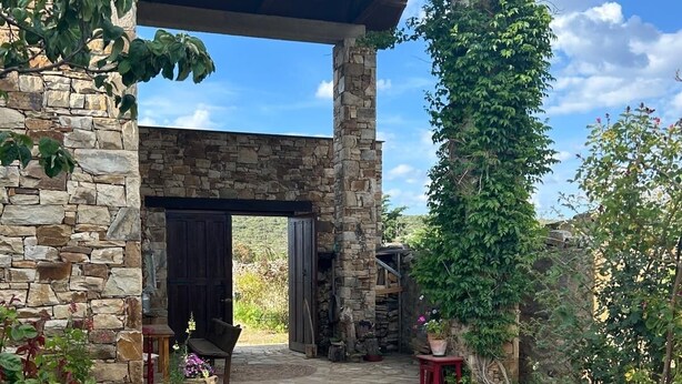 A stone patio with a covered seating area, stone walls, and potted plants.