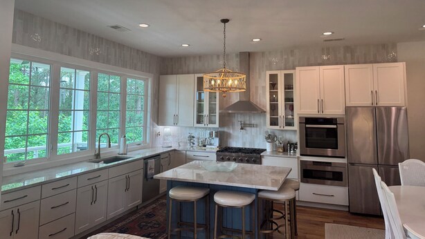 A modern kitchen with white cabinets, a stainless steel refrigerator, a gas stove, and a large window offering a view of greenery. - Oasis in Oxford - 4BR with an amazing view (Oxford)
