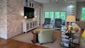 A spacious living room with a stone wall, a flat-screen TV, two armchairs, a sofa, and a coffee table. - Oasis in Oxford - 4BR with an amazing view (Oxford)
