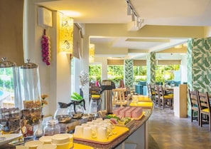 Enjoy a meal in our dining area, featuring a long counter with a variety of food and beverage options, artwork, and a view of the lush outdoor space.
