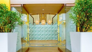 Ingresso moderno di un hotel con porta in vetro, parete decorata e scalinata in legno.