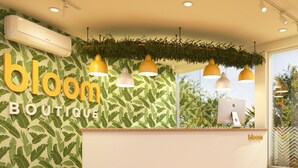 Una reception con insegna 'bloom boutique', circondata da vegetazione verde e illuminazione a sospensione.