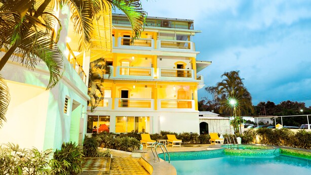 Un hotel a più piani con piscina, palme e facciata ben illuminata.
