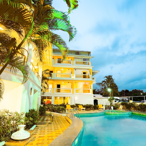 Hotel features a vibrant facade with balconies on each floor, overlooking a swimming pool and lush surroundings.