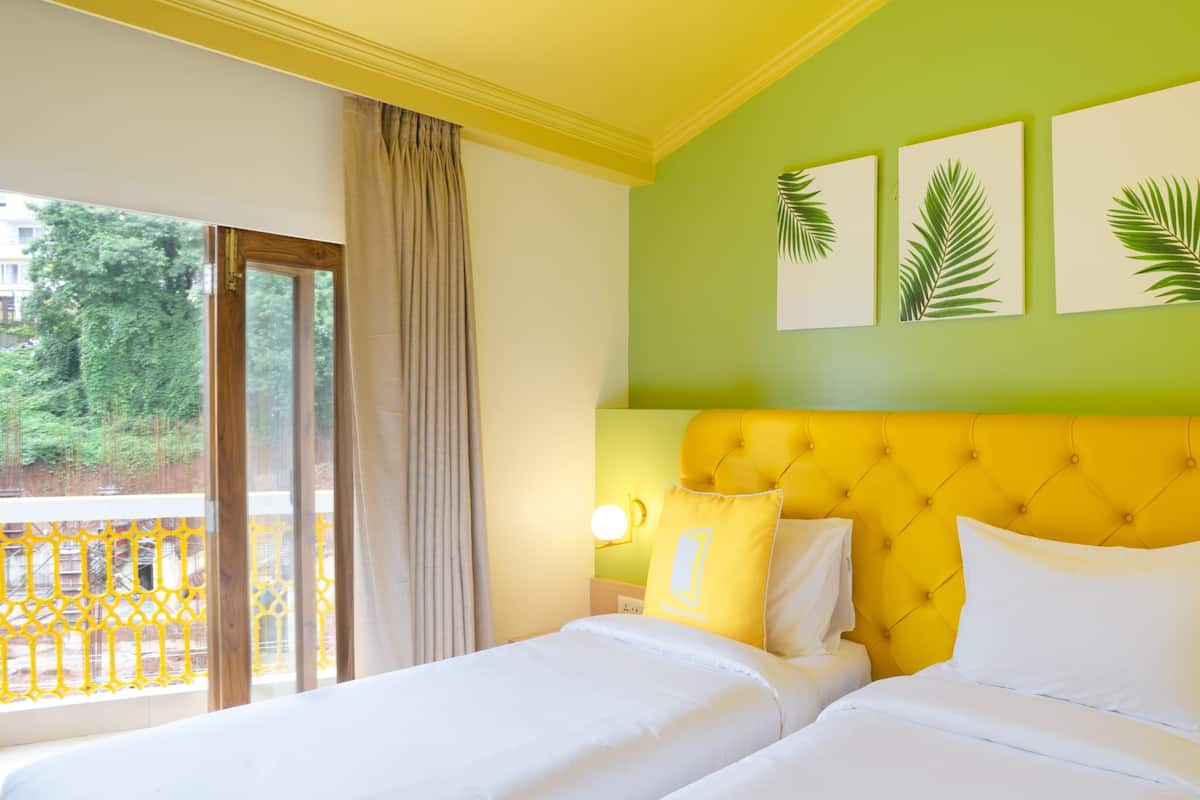 A hotel room with two beds, a yellow headboard, and a balcony with a view of greenery.