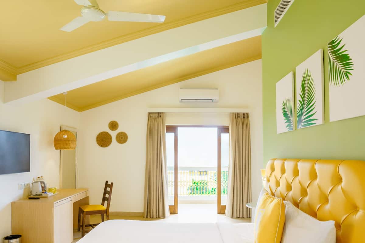 A hotel room with a bed, a desk, a chair, a television, and a balcony with curtains.