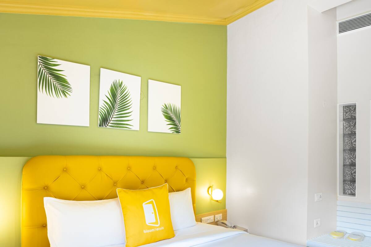 A hotel room with a yellow headboard, white bedding, and three palm leaf wall art pieces.