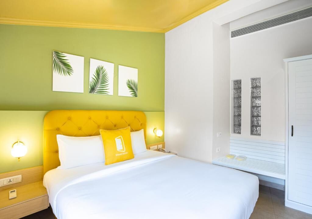 A hotel room with a bed, a nightstand, a wall-mounted lamp, and a window with a view.