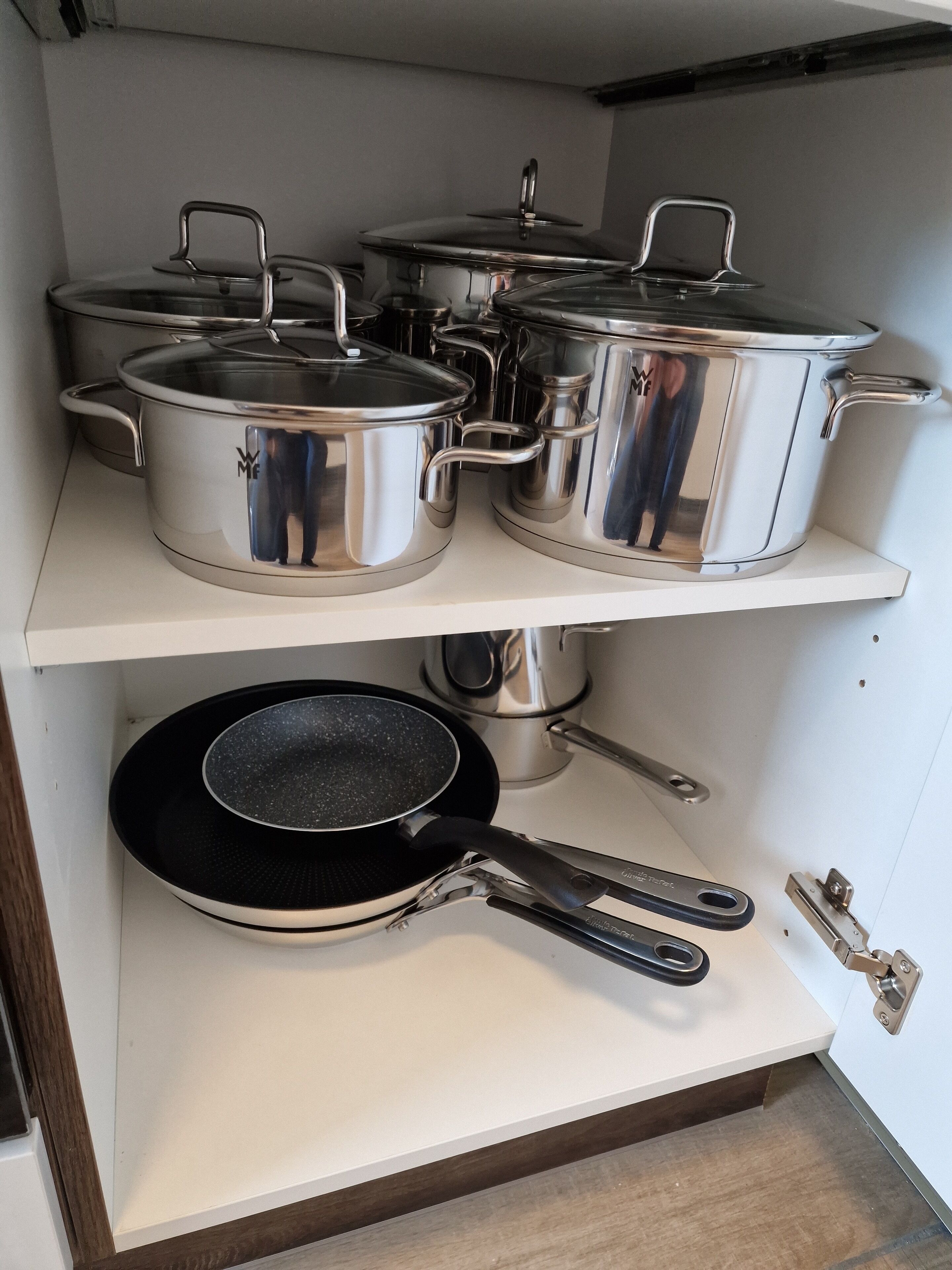 A kitchen with stainless steel cookware on shelves and a black frying pan on the countertop.