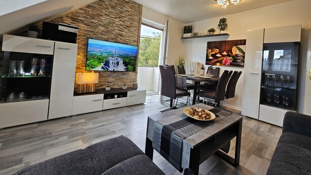 A modern kitchen with a flat-screen TV, dining area with chairs, and a built-in wine rack. - Bright and modern apartment in the attic very close to the centre and university (Kassel)