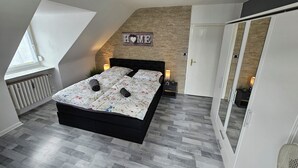 A bedroom with a bed, a stone wall, a radiator, a window, and a wardrobe. - Bright and modern apartment in the attic very close to the centre and university (Kassel)