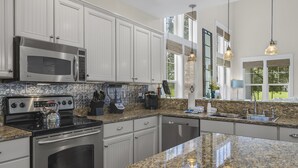 A modern kitchen with white cabinetry, stainless steel appliances, granite countertops, and large windows providing natural light. - Two Golf Carts ~ Golf Course Views ~ Pet Friendly (Miramar Beach)