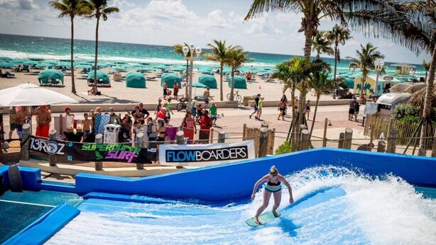 A water slide with a person surfing, surrounded by beach umbrellas and palm trees. - Hot Location-New Studio for 2-Beach-Margaritaville (Hollywood)