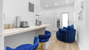 A modern kitchen with white countertops, a toaster, and a kettle. There are two blue bar stools and a blue cushioned seating area. - Hot Location-New Studio for 2-Beach-Margaritaville (Hollywood)