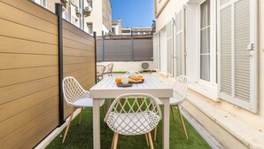 Un pequeño patio al aire libre con una mesa y sillas blancas, una valla de madera y vistas a la calle.
