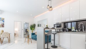 Una cocina moderna con armarios blancos, una isla central, taburetes de bar y una zona de comedor con una mesa y sillas.