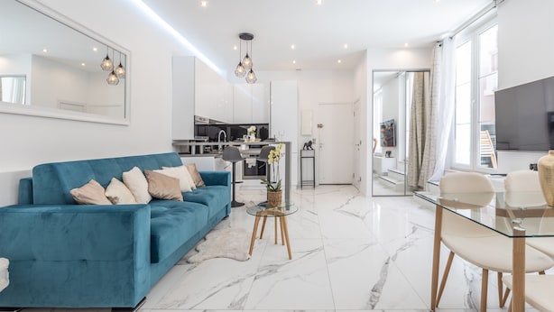 Una sala de estar moderna con un sofá azul, una mesa de centro de vidrio y un comedor con mesa y sillas de vidrio.