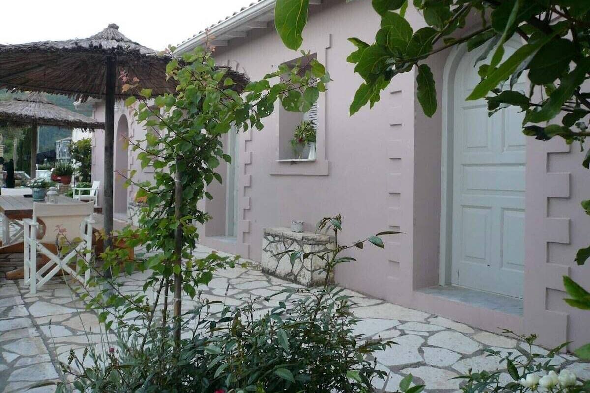 A pink building with a stone-paved patio, a white door, and a small window.