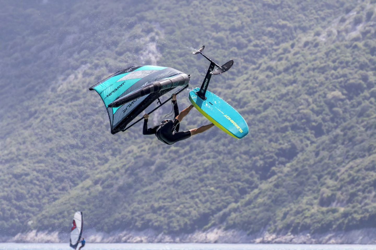 Une personne pratiquant le kitesurf au-dessus de l’eau, avec une chaîne de montagnes en arrière-plan.