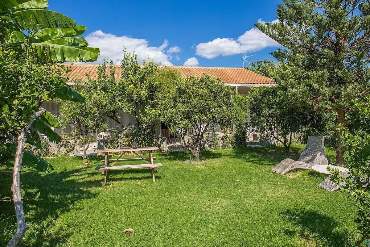Une cour arrière verdoyante avec une table de pique-nique en bois, un banc en pierre et un petit arbre.